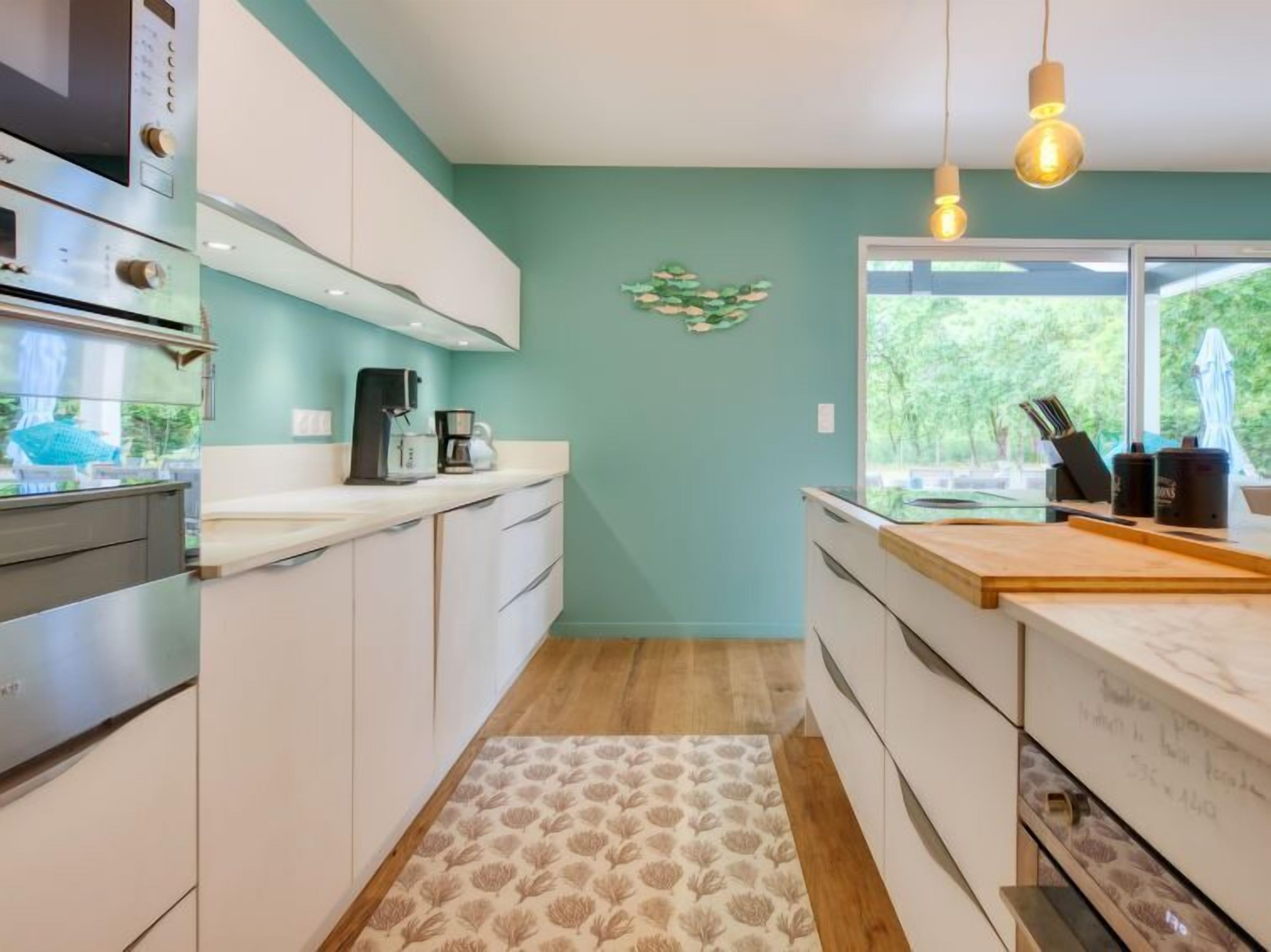 Une cuisine moderne avec des meubles blancs, une machine à café et une vue sur la verdure environnante.