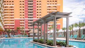 A hotel pool area with a large building in the background, lounge chairs, and a covered seating area. - The Calypso Resort in PCB , Family Friendly,11 Floor, Free Beach Chairs Service (Panama City Beach)