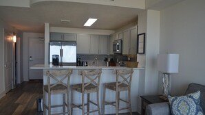 A modern kitchen with a central island, bar stools, a refrigerator, and a microwave. - The Calypso Resort in PCB , Family Friendly,11 Floor, Free Beach Chairs Service (Panama City Beach)