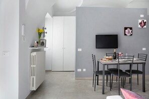 Eine moderne Küche mit weißen Schränken, einem weißen Heizkörper und einem Essbereich mit Tisch, Stühlen und einem Flachbildfernseher.