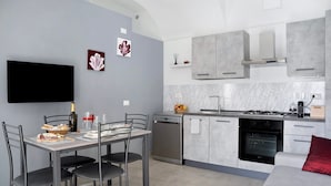 A modern kitchen with grey cabinets, a built-in oven, and a dining area with a table set for two. - Holiday Apartment "Casa Vacanze La Porta in Piazza" with Terrace (guarene)