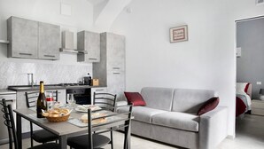 A modern kitchen with grey cabinets, a dining table with chairs, and a grey sofa with red cushions. - Holiday Apartment "Casa Vacanze La Porta in Piazza" with Terrace (guarene)