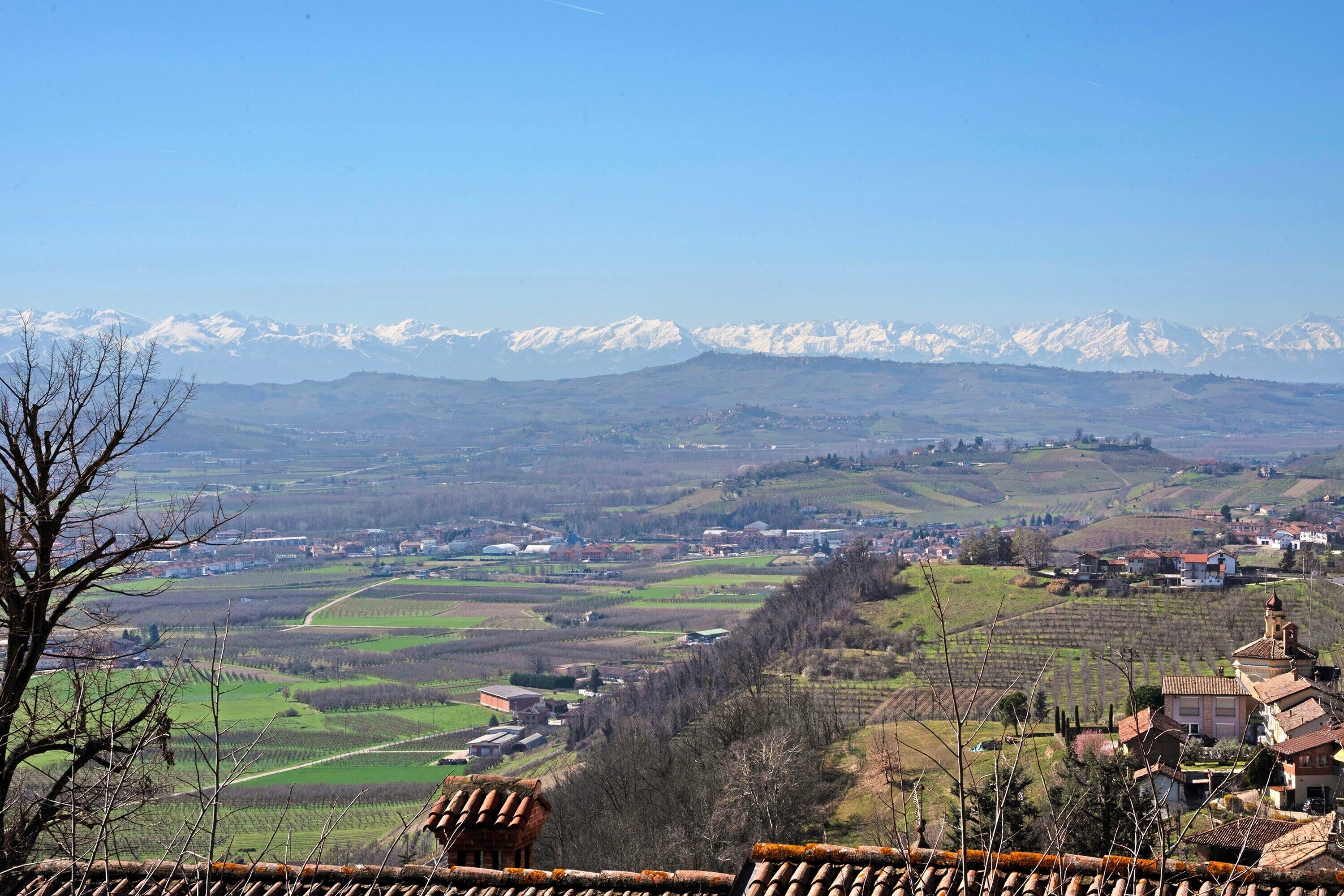 A panoramic view of a valley with a town, mountains in the background, and a traditional building with a tiled roof in the foreground.
