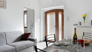 A modern living room with a grey sofa, a dining table set with plates, glasses, and a bottle. - Holiday Apartment "Casa Vacanze La Porta in Piazza" with Terrace (guarene)