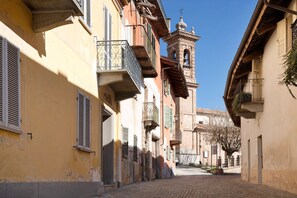 A narrow cobblestone street lined with historic buildings, a bell tower, and balconies with wrought iron railings. - Holiday Apartment "Casa Vacanze La Porta in Piazza" with Terrace (guarene)