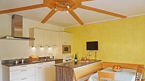 A kitchen with wooden beams, white cabinets, a wooden island, and a dining area with a table and chairs. - Apartment "Huterhof Wiesengrund 2" with Mountain View, Balcony & Wi-Fi (Sarentino)