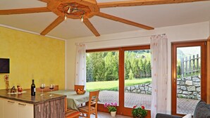 A kitchen with a wooden ceiling, a dining area with a table and chairs, a sofa, and a view of a garden through a glass door. - Apartment "Huterhof Wiesengrund 2" with Mountain View, Balcony & Wi-Fi (Sarentino)