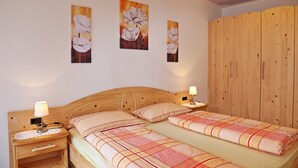 A bedroom with two beds, wooden headboard, bedside lamps, and wall-mounted paintings. - Apartment "Huterhof Wiesengrund 2" with Mountain View, Balcony & Wi-Fi (Sarentino)