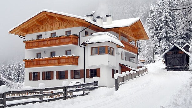 A multi-story building with balconies, a wooden facade, and a snow-covered landscape. - Apartment "Huterhof Wiesengrund 2" with Mountain View, Balcony & Wi-Fi (Sarentino)