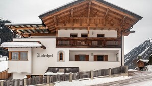 A two-story building with a wooden balcony, a sign reading 'Huterhof,' and a snow-covered landscape.