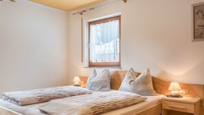 A bedroom with a wooden bed, two bedside tables, a window with lace curtains, and a wall-mounted picture.