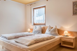 A bedroom with a wooden bed, two bedside tables, a window with lace curtains, and a wall-mounted picture.