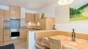 A modern kitchen with wooden cabinets, a built-in oven, and a dining area with a table and chairs.