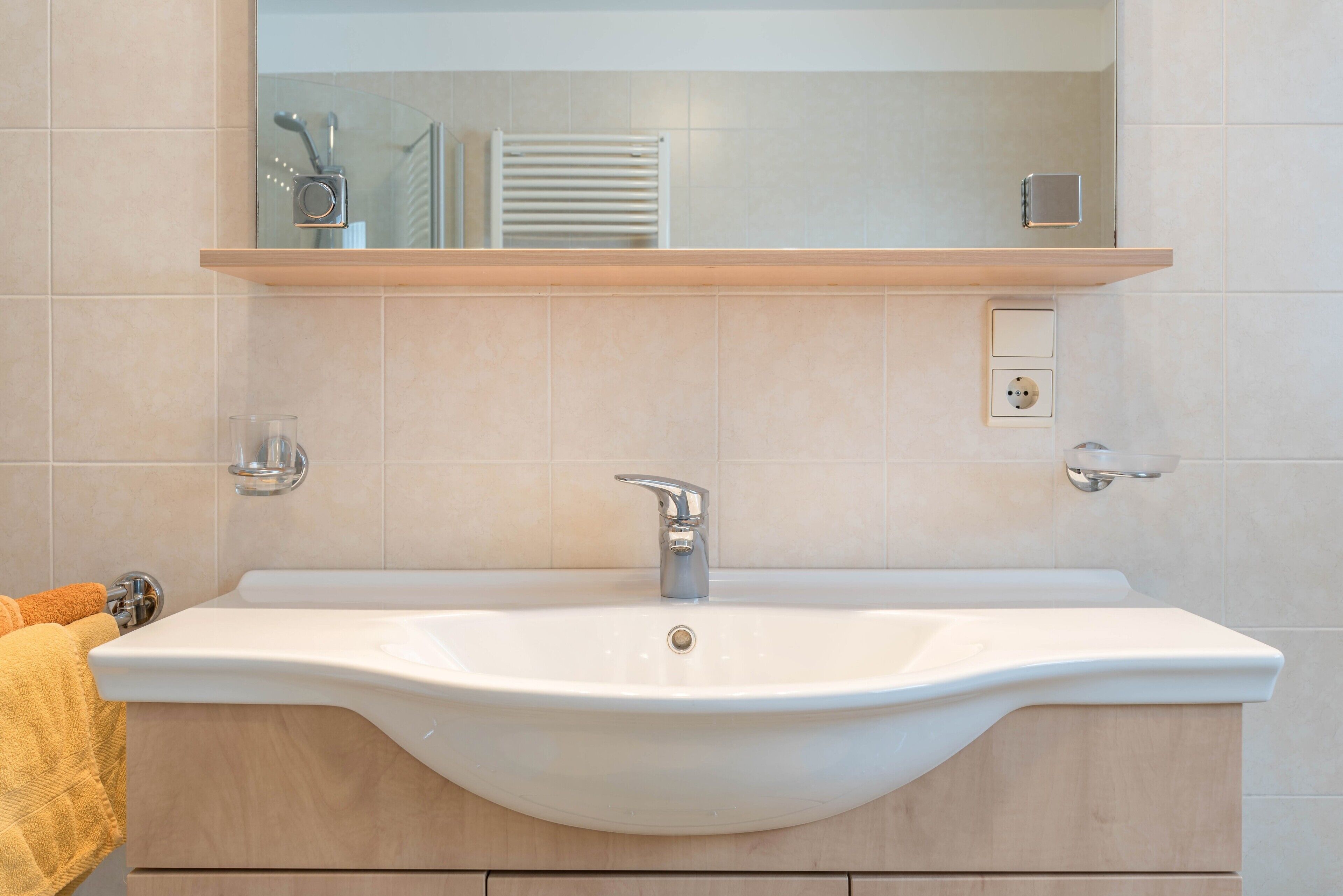 Une salle de bain avec un lavabo blanc, un miroir au-dessus et une serviette accrochée sur le côté gauche.