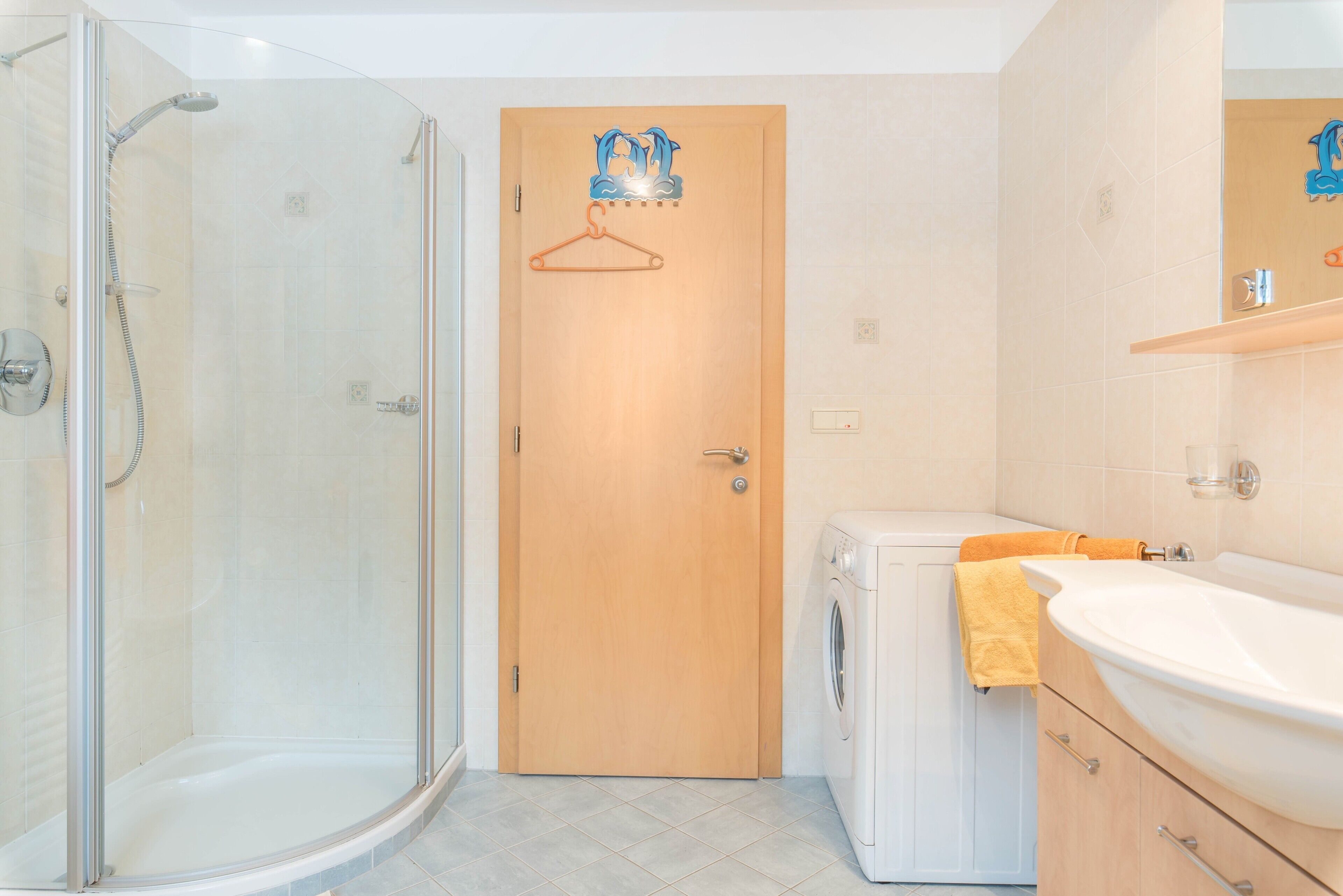 Ein Badezimmer mit einer Duschkabine, einer Holztür, einer Waschmaschine und einem Waschbecken mit Spiegel.