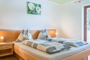 A double bed with a patterned bedspread and pillows, a bedside table with a lamp, and a wall-mounted painting.