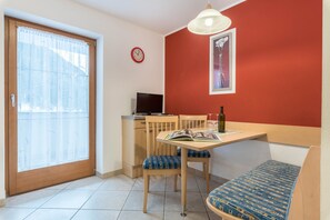 A room with a dining table, chairs, a sofa, a TV, a clock, and a window with curtains.
