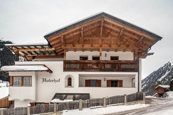A two-story building with a wooden balcony, a sign reading 'Huterhof,' and a snow-covered landscape.