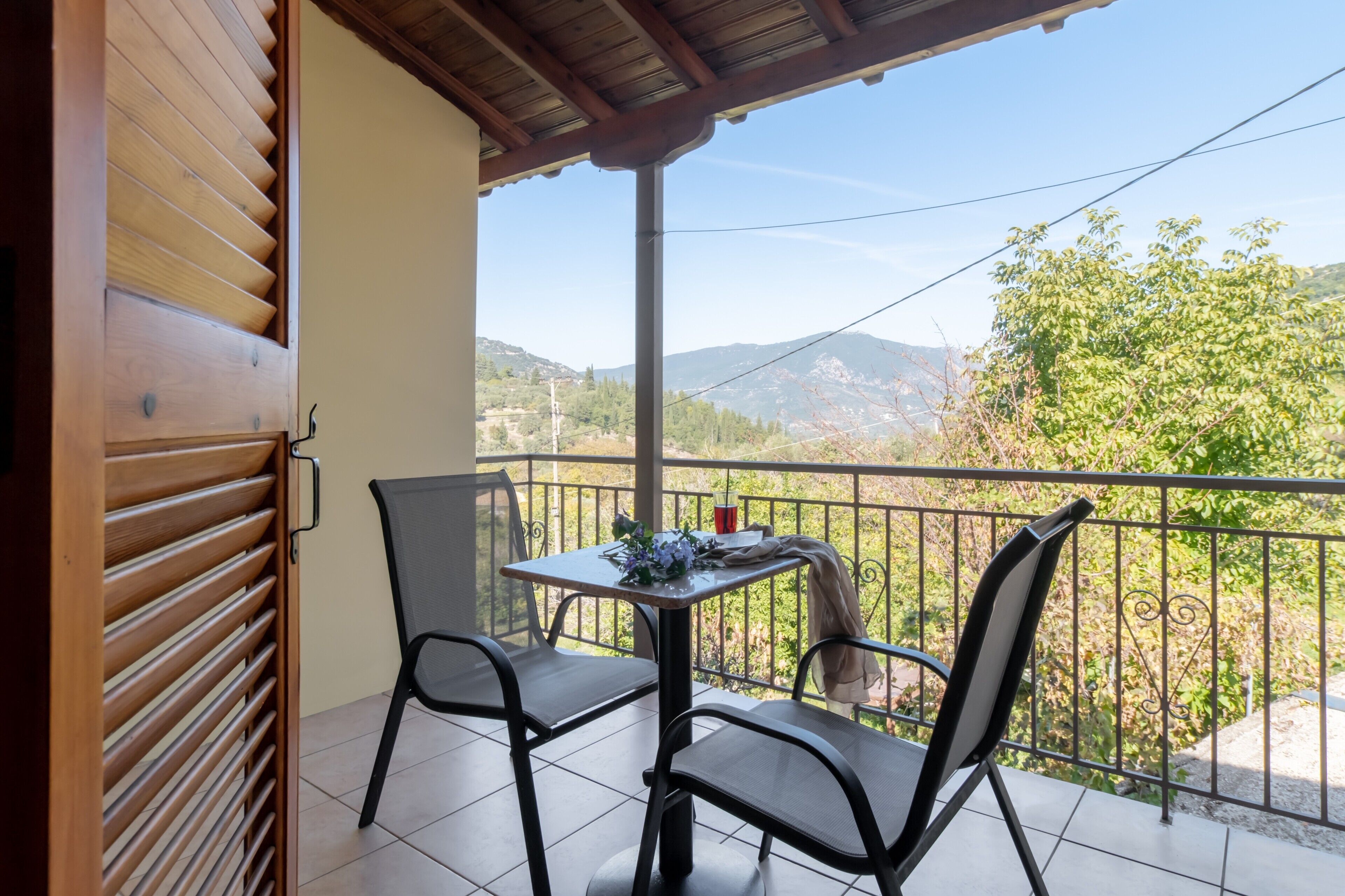 A balcony with a table and chairs, a view of the countryside, and a wooden door.