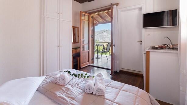 Une chambre avec un lit, un téléviseur fixé au mur et une porte donnant sur un espace extérieur.
