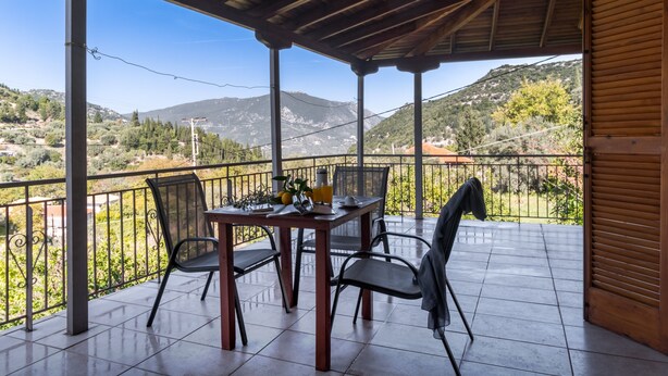 Eine überdachte Terrasse mit Tisch und Stühlen und Blick auf die Landschaft, sowie eine Holztür.