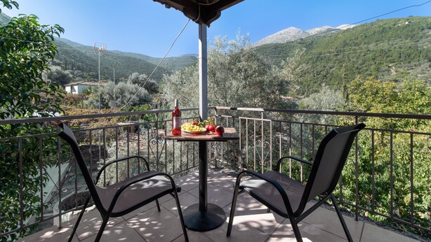 Ein Balkon mit zwei Stühlen, einem Tisch mit Obst und Blick auf Berge.