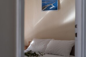 Une chambre à coucher avec un lit, des oreillers, une table de chevet, un tableau encadré au mur et une plante sur le lit.