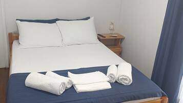 Una cama individual con estructura de madera, ropa de cama blanca y dos toallas enrolladas.