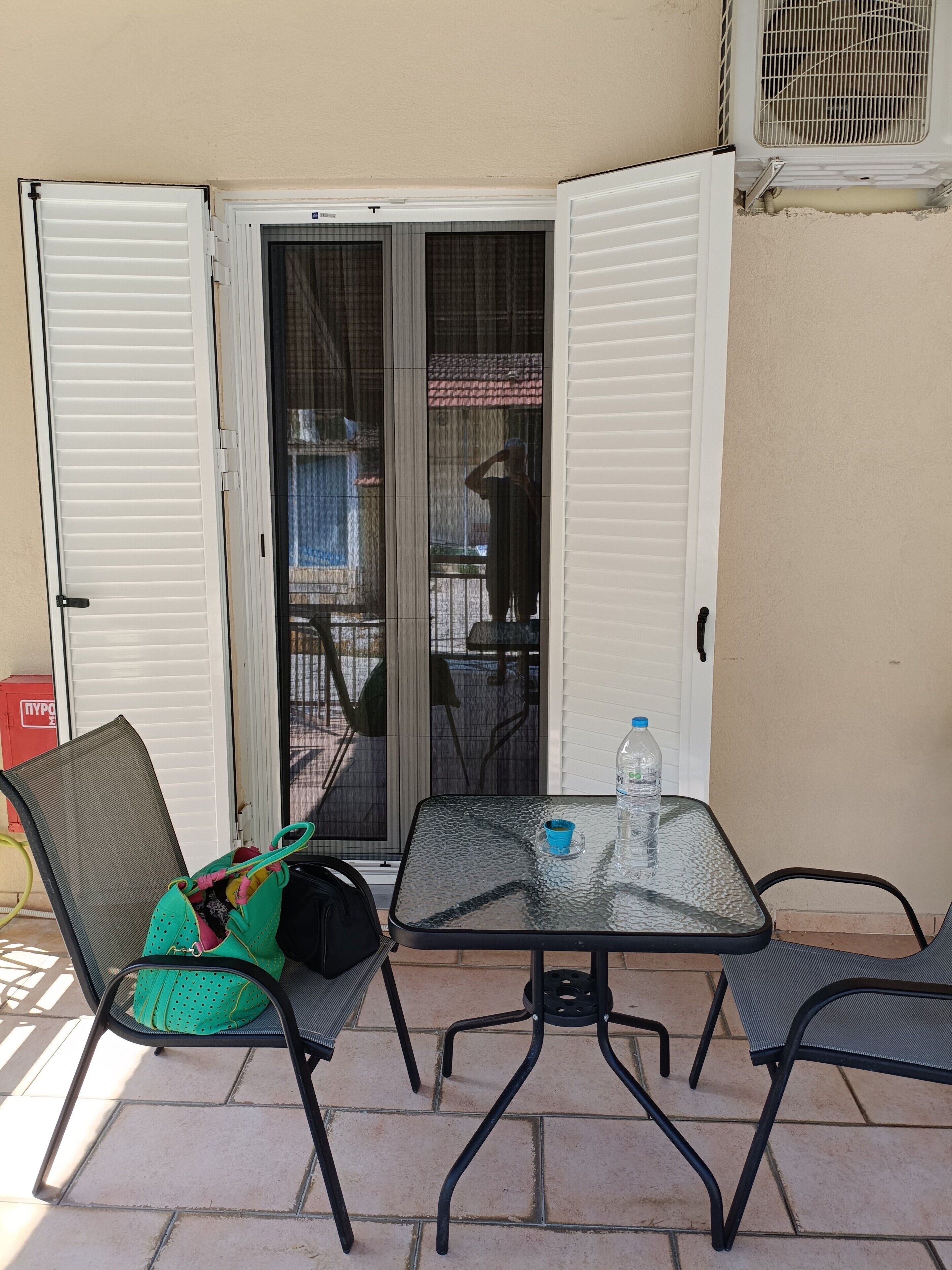 Une terrasse extérieure avec une table et des chaises, une bouteille d’eau et un sac vert.
