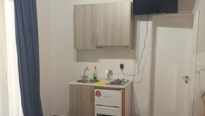 Pieni hotellihuone, jossa on sänky, pieni keittokomero, televisio ja ovi.