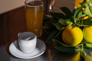 A white cup on a saucer, a glass of yellow liquid, and lemons on a table.