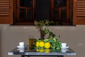A table with lemons, a glass of juice, and two cups, set against a window with wooden shutters.