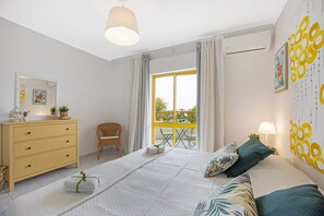 A bedroom with a bed, dresser, chair, and a window with a view.