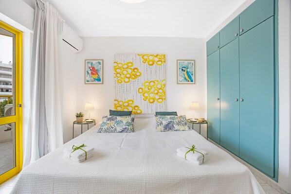 A hotel room with a bed, two side tables, a wall art piece, a wardrobe, and a view through a window.
