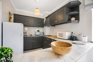 A modern kitchen with dark cabinets, a white refrigerator, a wooden bowl on the counter, and a hanging light fixture.