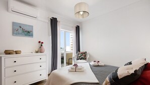 A bedroom with a bed, a dresser, a chair, a painting, and a window. - Apartment "Casa Farol" with Sea View, Balcony & Wi-Fi (Portimão)