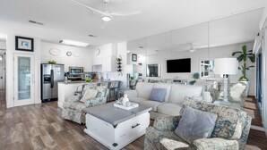 A modern living room with a sofa, armchairs, and a coffee table. There is a kitchen area with appliances and a dining table. - Beachfront Condo + Bikes, Community Pool & Views (Santa Rosa Beach)