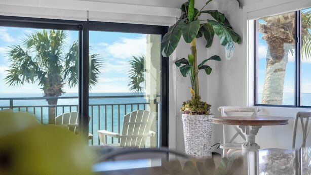 A balcony with a view of the ocean, white chairs, a table, and a large plant. - Beachfront Condo + Bikes, Community Pool & Views (Santa Rosa Beach)