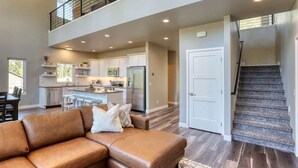 A spacious living area with a brown leather sofa, a kitchen with white cabinets, and a staircase. - Sunset Ridge (Lead)