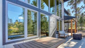 A modern outdoor patio with a wooden bench, large windows, and a covered seating area. - Sunset Ridge (Lead)