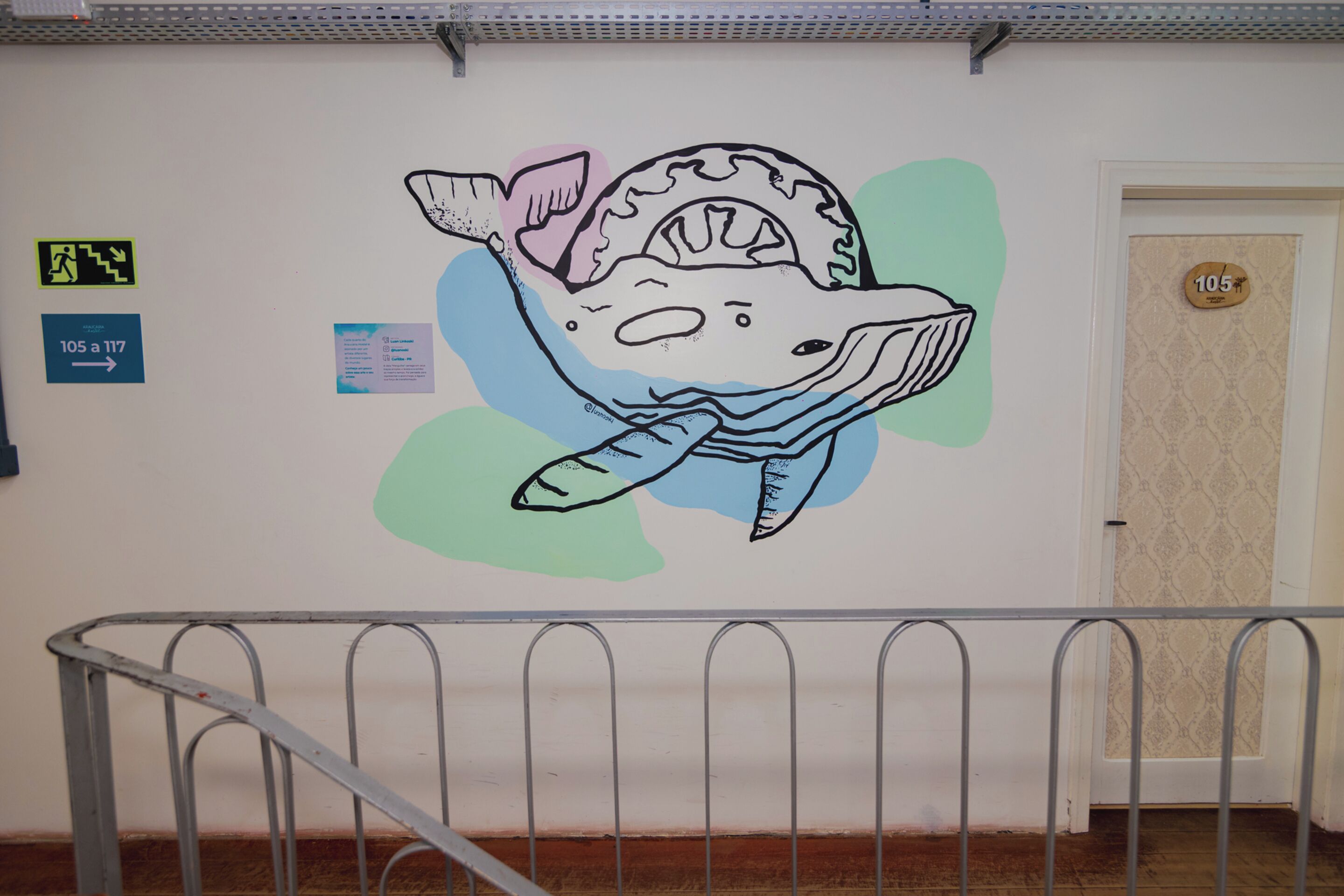 Pared con un dibujo grande y colorido de un pez, señales de dirección y una puerta con el número 105.