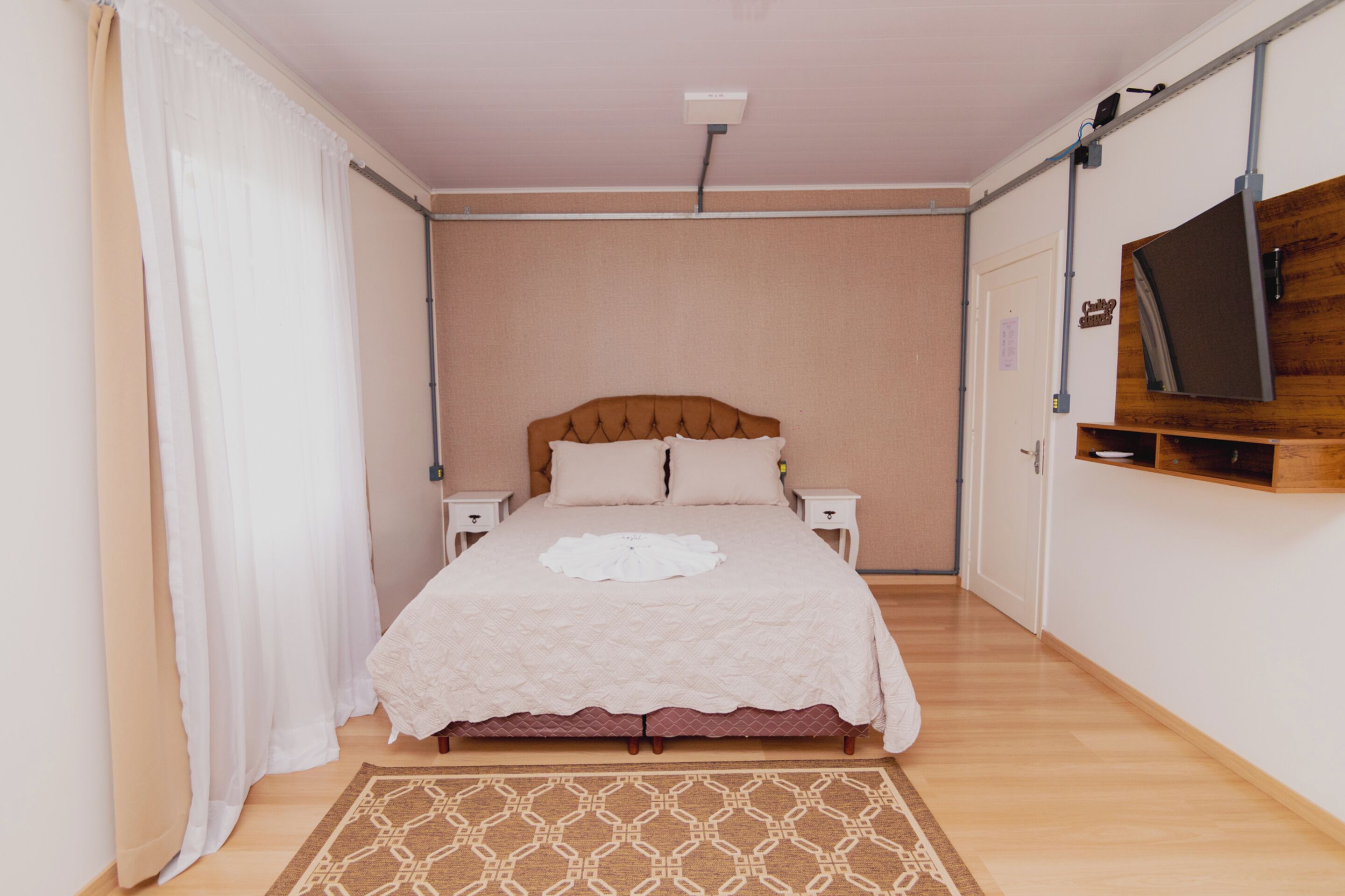 A neatly arranged bedroom with a bed, bedside tables, a TV mounted on the wall, and a patterned rug.