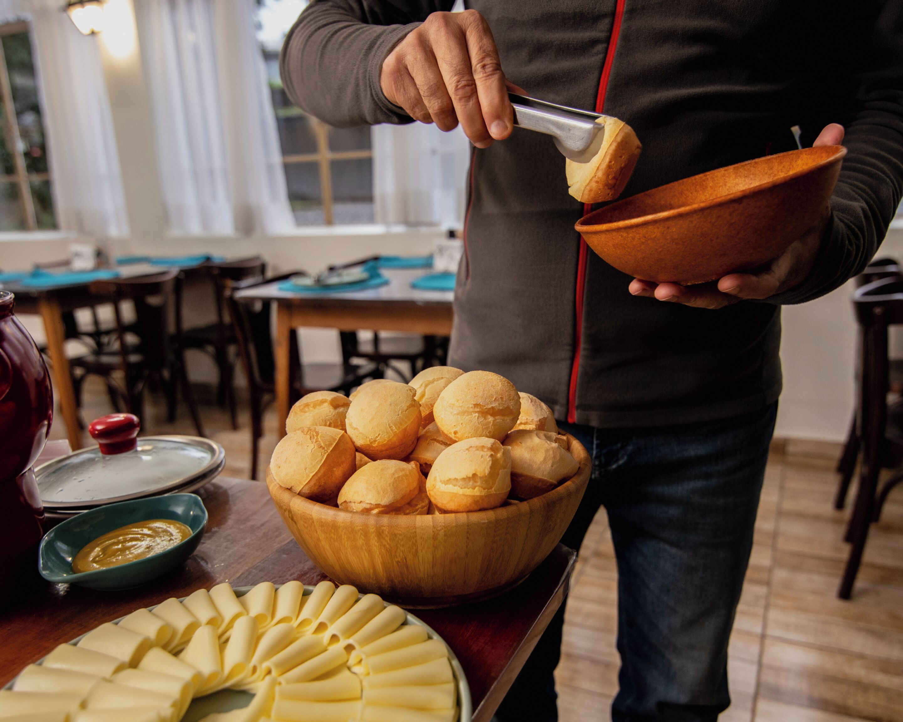 Una persona sosteniendo un bol de panecillos, un plato de queso en rodajas y un bol de salsa.