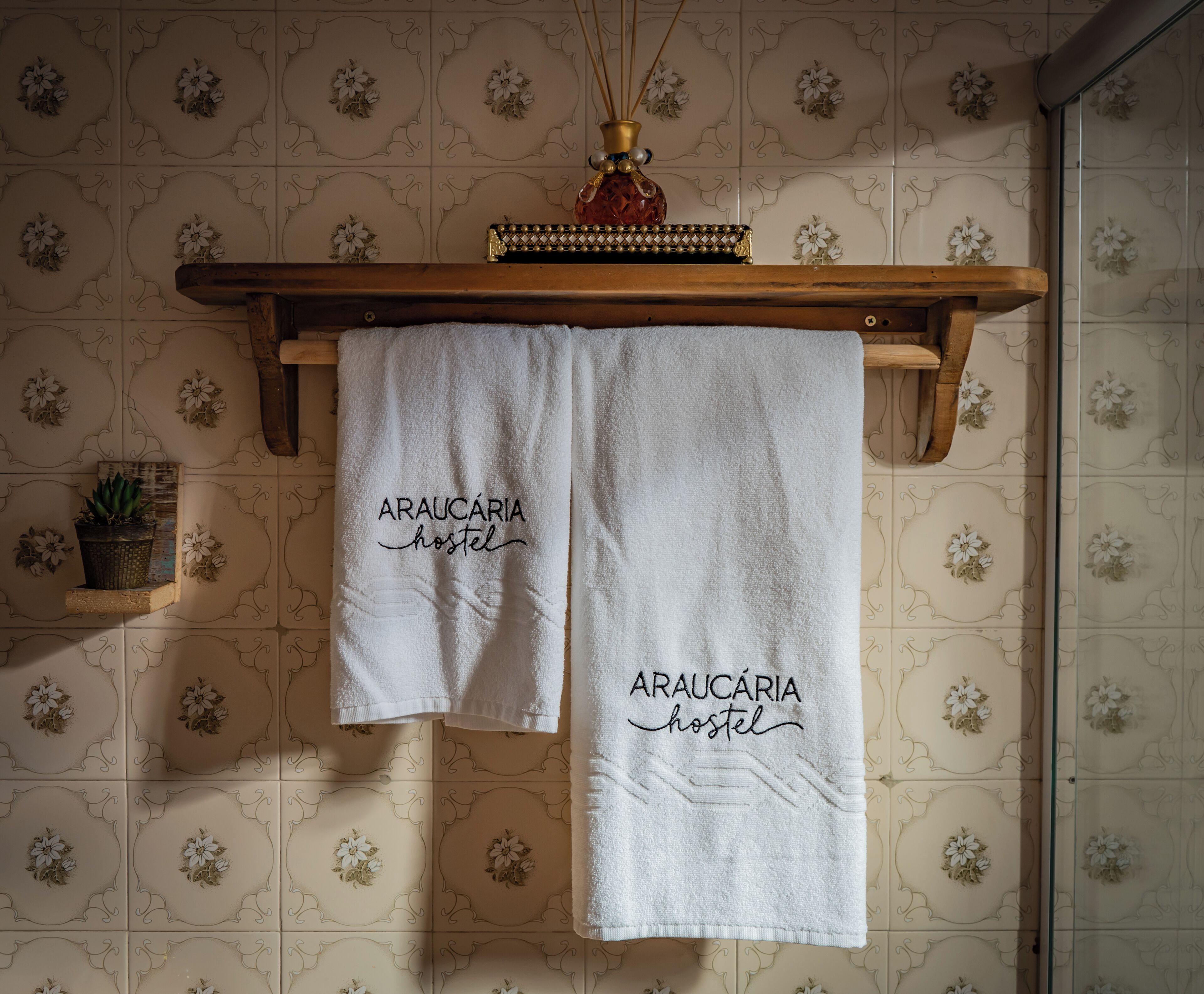 Two white towels hanging on a wooden rack with the text "Arauçária hostel" printed on them.