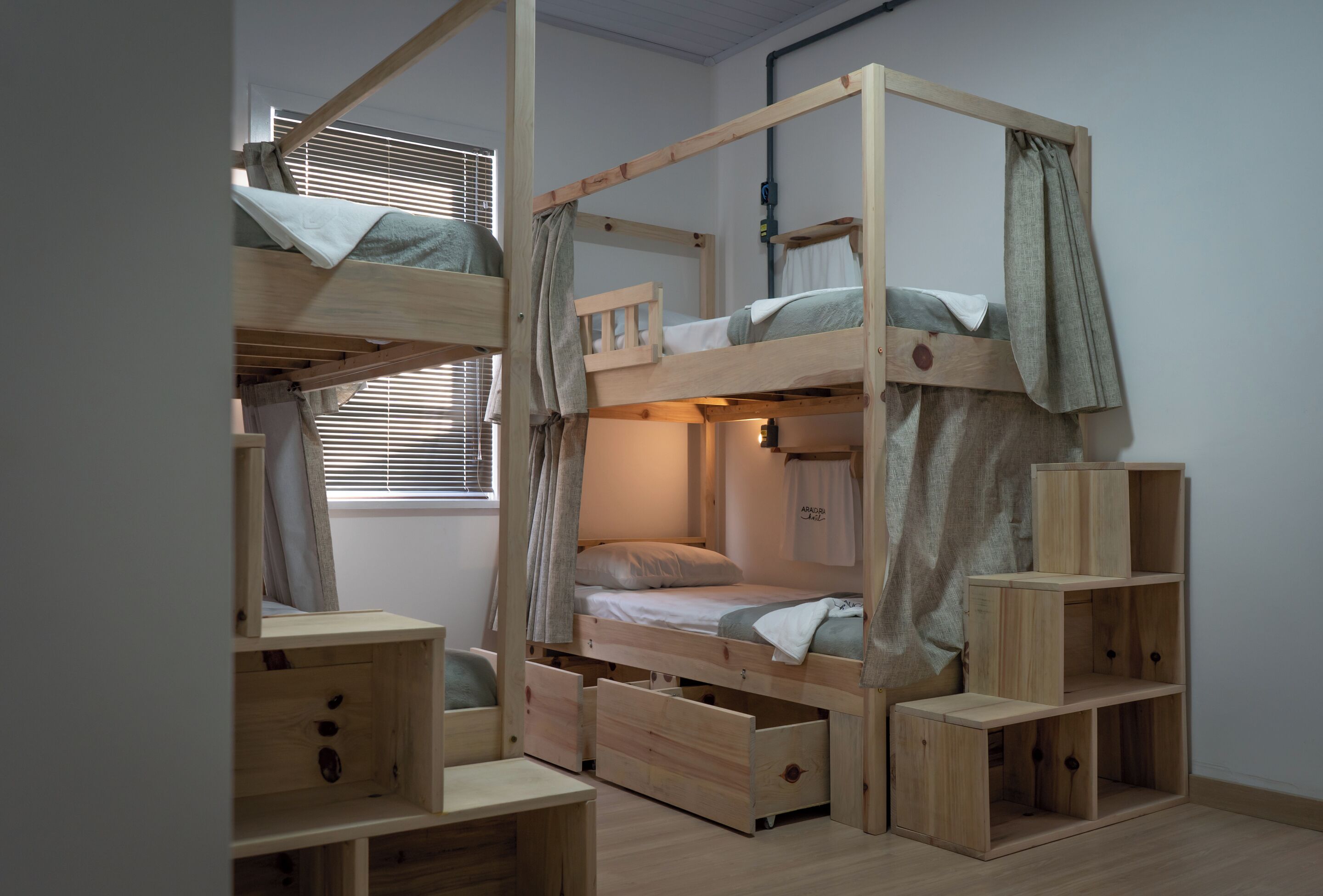 A bunk bed with a wooden frame, a desk, and a shelving unit in a room with a window.
