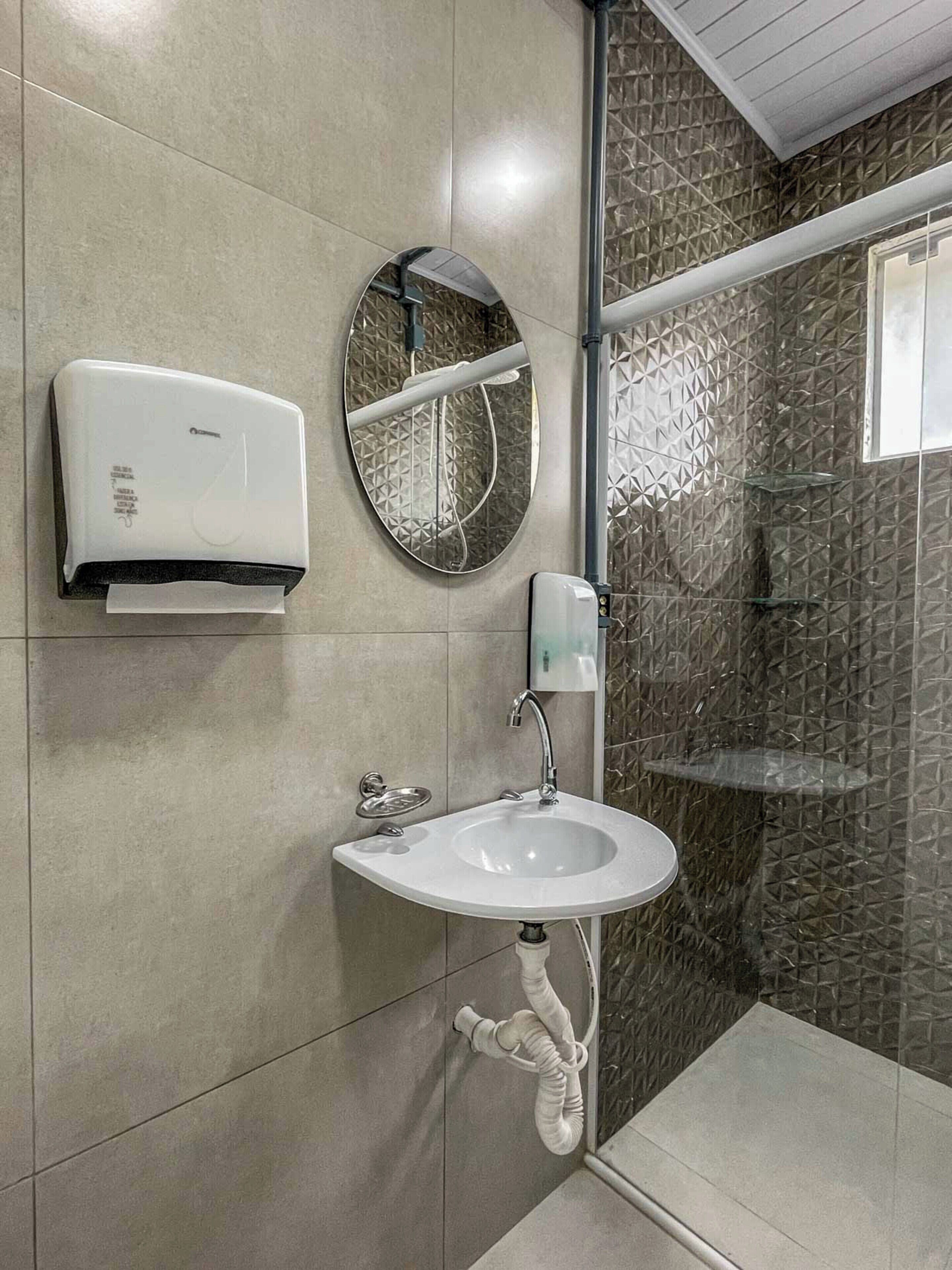 A bathroom with a white sink, a mirror, a hand dryer, and a shower area with a textured wall.