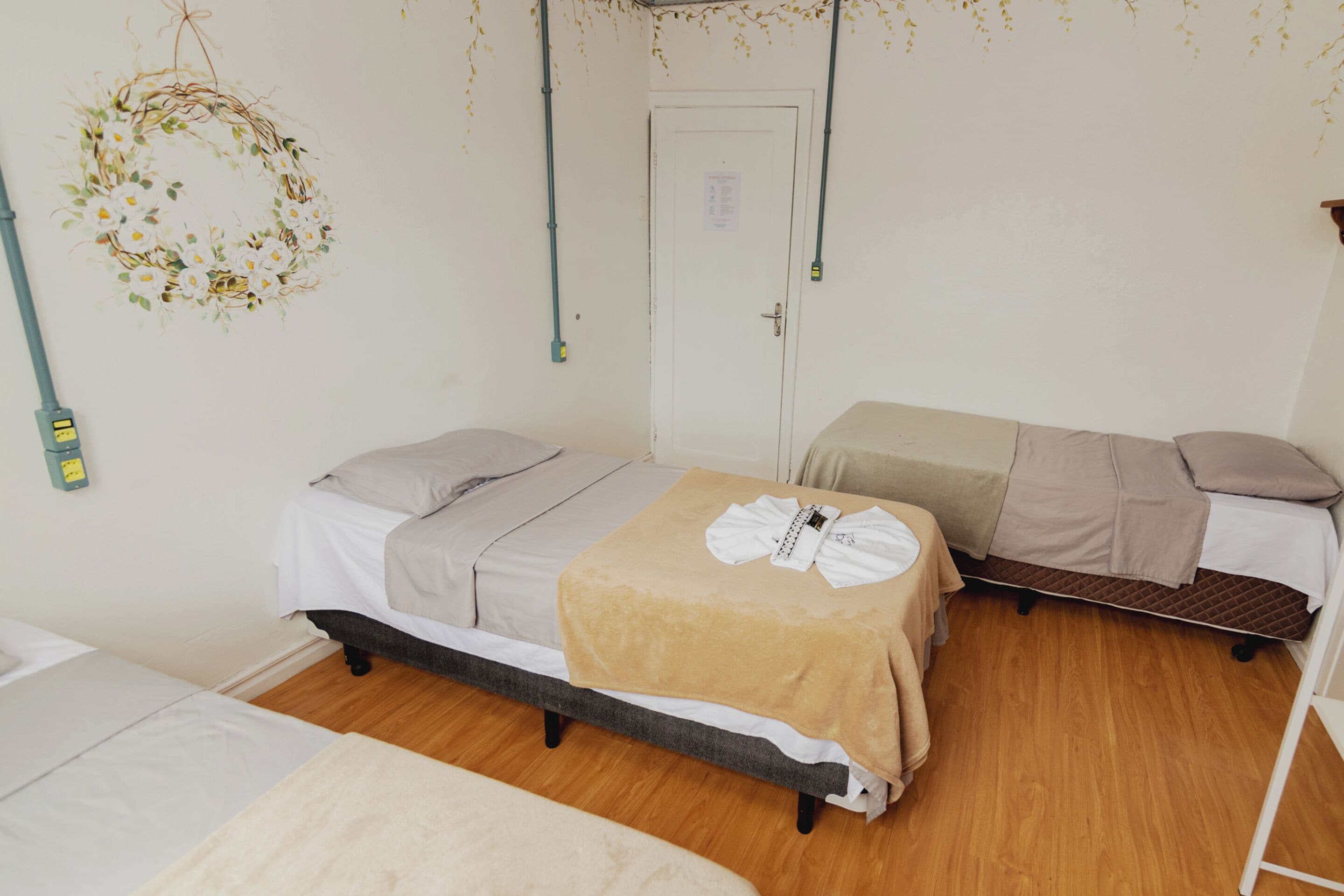 A room with two beds, a wooden floor, and a door with a sign.
