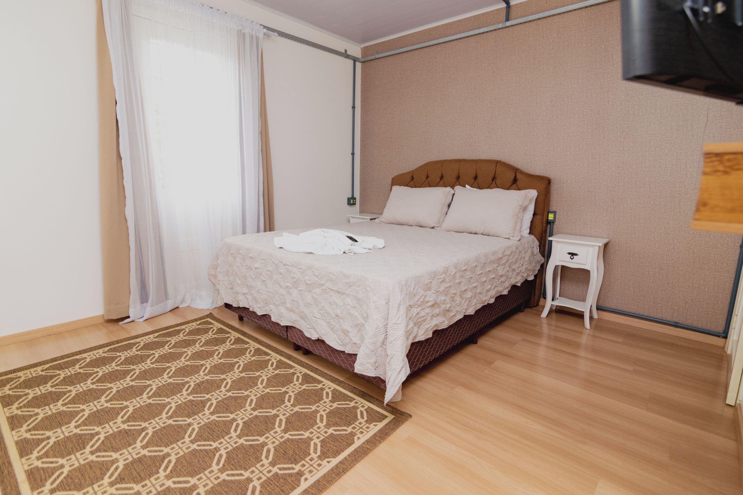 Un dormitorio ordenado con cama, mesita de noche y alfombra estampada.