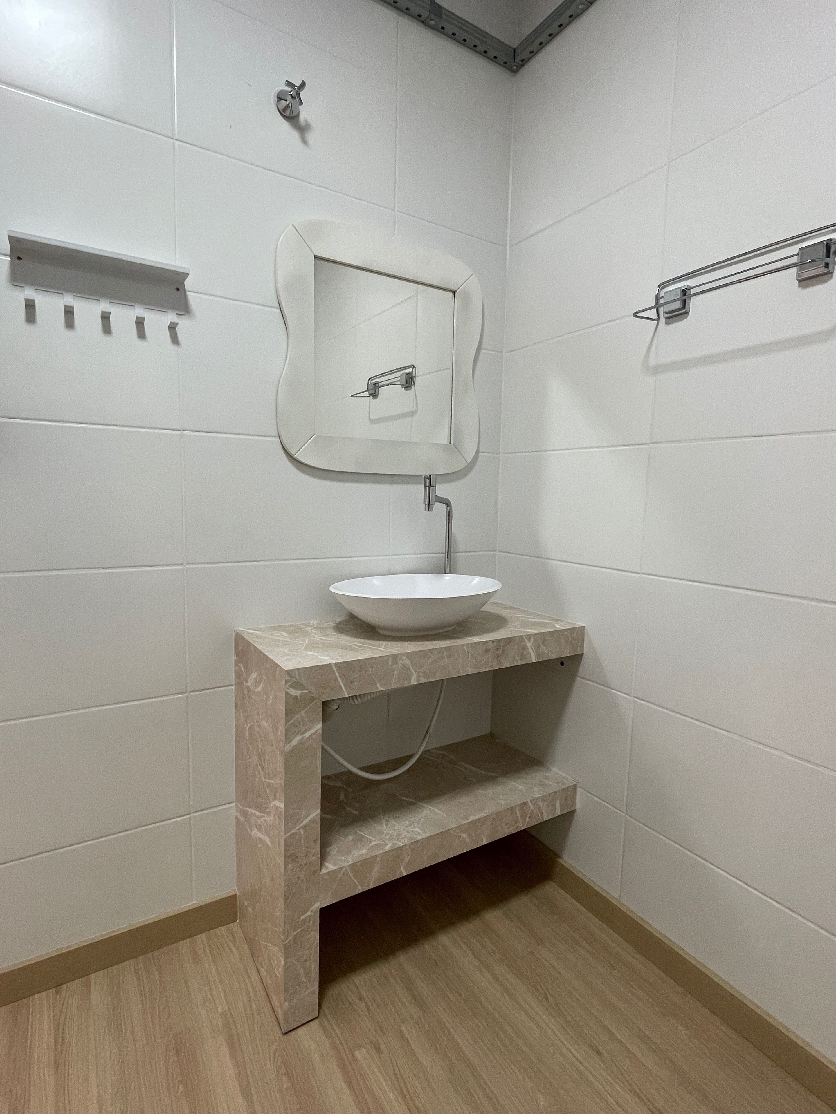 A bathroom with white tiled walls, a marble vanity with a sink, and a mirror.
