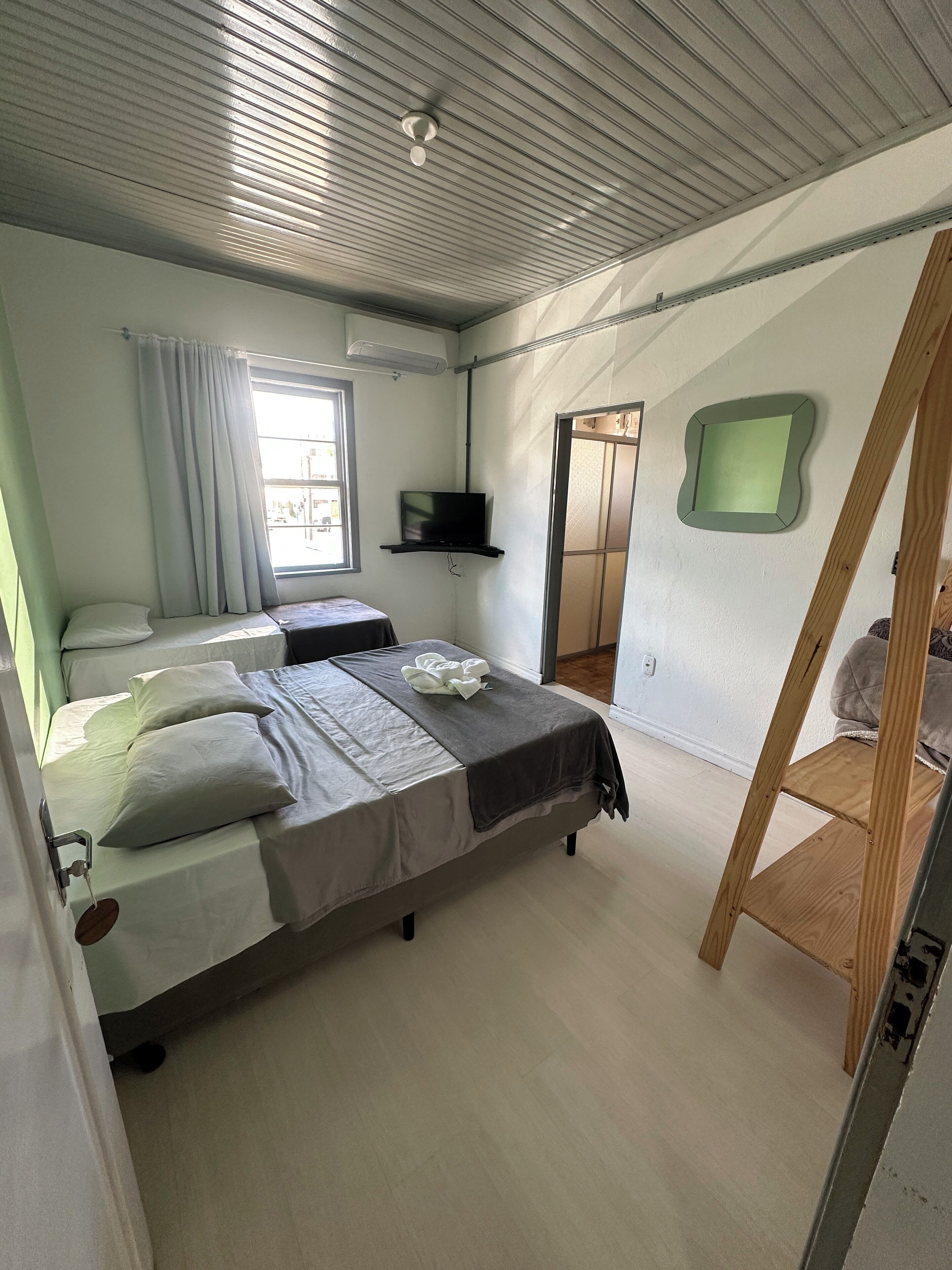 A bedroom with a bed, a TV mounted on the wall, a window with curtains, and a wooden ladder.
